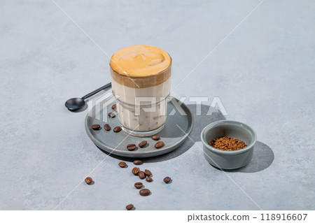 Dalgona coffee. Whipped instant coffee in a glass on a plate with coffee beans on a blue background. 118916607