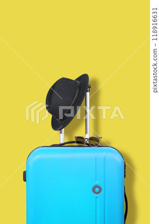 Blue suitcase and black hat on a yellow background. Blue suitcase and black hat on a yellow background. 118916631