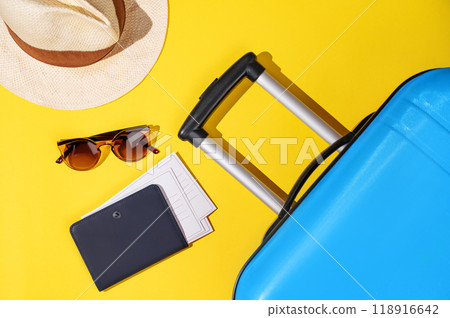 Flat lay blue suitcase with travel accessories, hat and sunglasses on a yellow background. Flat lay blue suitcase with travel accessories, hat and sunglasses on a yellow background. 118916642