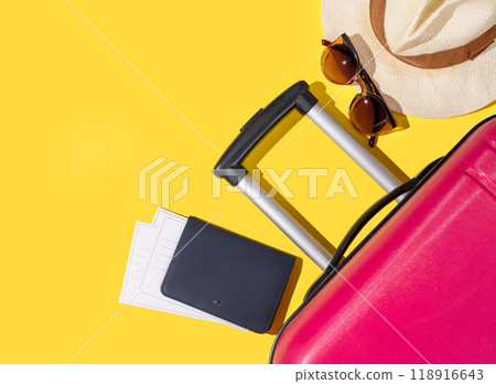 Flat lay pink suitcase with travel accessories, hat and sunglasses on a yellow background. Flat lay pink suitcase with travel accessories, hat and sunglasses on a yellow background. 118916643