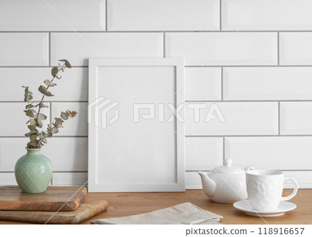 A  frame with a blank canvas against a white tile wall and on a wooden tabletop 118916657