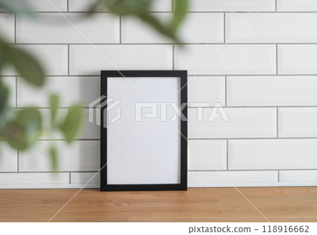 A black frame with a blank canvas against a white tile wall and on a wooden tabletop A black frame with a blank canvas against a white tile wall and on a wooden tabletop 118916662