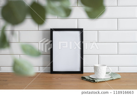 A black frame with a blank canvas against a white tile wall and on a wooden tabletop A black frame with a blank canvas against a white tile wall and on a wooden tabletop 118916663