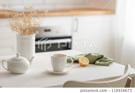 A cup of tea with lemon and a teapot on a white table with dry bouquet. 118916673