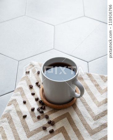 A cup of black coffee on a napkin on a trendy gray tile background with coffee beans  118916766
