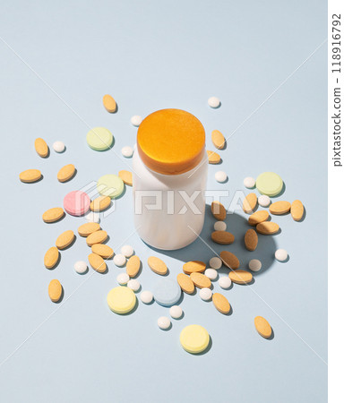 Assorted pills and nutritional supplements in different colors with bottle on blue background. Assorted pills and nutritional supplements in different colors with bottle on blue background. 118916792