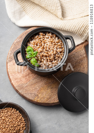 Buckwheat porridge in a black pan on a cutting board on a light background with raw grains in a bowl Buckwheat porridge in a black pan on a cutting board on a light background with raw grains in a bowl 118916813