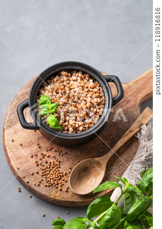 Buckwheat porridge in a black pan on a cutting board on a light background with raw grains Buckwheat porridge in a black pan on a cutting board on a light background with raw grains 118916816