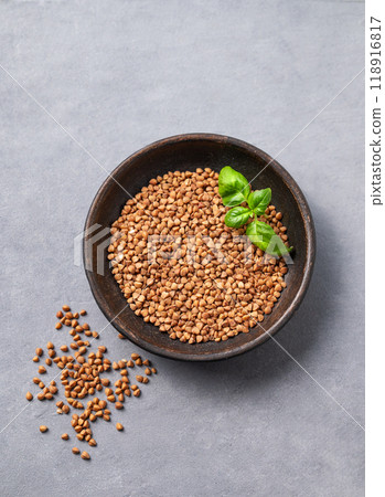 Raw buckwheat grains with fresh herbs in a wooden bowl on a light background. Raw buckwheat grains with fresh herbs in a wooden bowl on a light background. 118916817