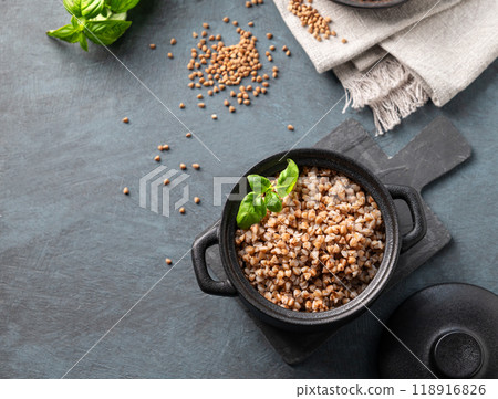 Buckwheat porridge in a black pan on a dark  background with raw grains and herbs. 118916826