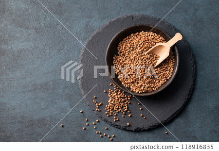 Raw buckwheat grains in a wooden bowl on a board on a dark background. Raw buckwheat grains in a wooden bowl on a board on a dark background. 118916835