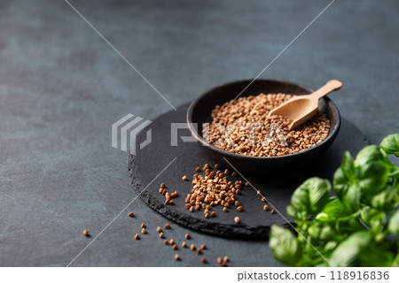 Raw buckwheat grains in a wooden bowl on a board on a dark background with fresh herb. 118916836