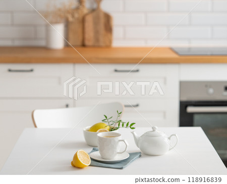 A cup of tea with lemon and a teapot on a white table. A cup of tea with lemon and a teapot on a white table. 118916839