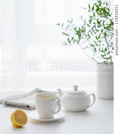 A cup of tea with lemon, a teapot and green branch on a white table against the background A cup of tea with lemon, a teapot and green branch on a white table against the background 118916851