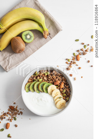 Granola and milk product with banana and kiwi on a white table. 118916864