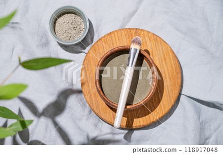 Organic cosmetic blue clay in a bowl with a brush on a wooden board on linen background with shadow Organic cosmetic blue clay in a bowl with a brush on a wooden board on linen background with shadow 118917048