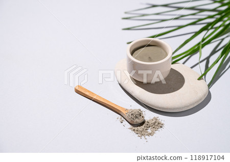 Blue clay in a bowl and spoon on a stone on a light background with palm leaves and shadow. Blue clay in a bowl and spoon on a stone on a light background with palm leaves and shadow. 118917104