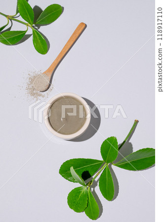 Blue clay in a bowl and spoon on a light background with leaves and shadow. 118917110