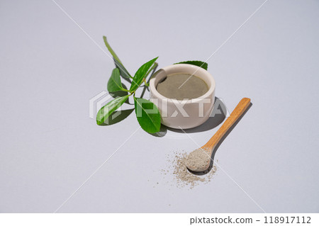 Spa treatment. Blue clay in a bowl and spoon on a light background with leaves and shadow. Spa treatment. Blue clay in a bowl and spoon on a light background with leaves and shadow. 118917112
