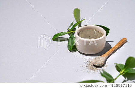 Spa treatment. Blue clay in a bowl and spoon on a light background with leaves and shadow. Spa treatment. Blue clay in a bowl and spoon on a light background with leaves and shadow. 118917113