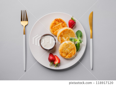 Cottage cheese, cheesecakes or syrniki with strawberries, sour cream and mint leaves on white plate Cottage cheese, cheesecakes or syrniki with strawberries, sour cream and mint leaves on white plate 118917120