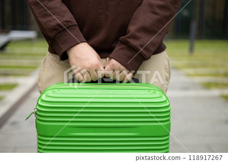 Traveler walking with a suitcase, traveling in the city, cropped view with no face. Passenger waiting at bus station or near hotel. Selective focus on hands holding baggage 118917267