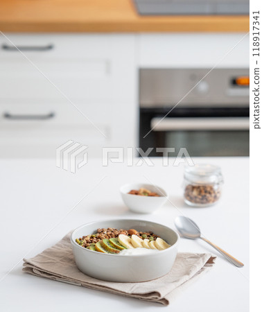 Baked granola with banana and kiwi on the table on a white kitchen background. Baked granola with banana and kiwi on the table on a white kitchen background. 118917341