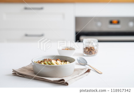 Baked granola with banana and kiwi on the table on a white kitchen background close up. 118917342