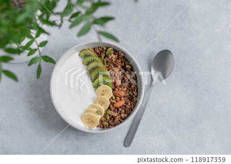 Healthy granola with yogurt, banana and kiwi in a bowl on a blue background with branch. Healthy granola with yogurt, banana and kiwi in a bowl on a blue background with branch. 118917359