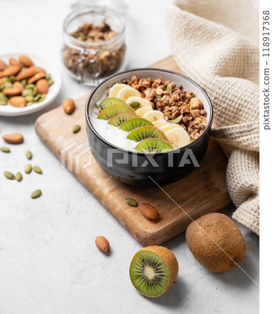 Muesli with yogurt, banana and kiwi in a bowl on a cutting board on a light background 118917368