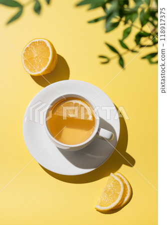 Herbal tea with lemon in a white cup on a yellow background with citrus fruit and slices. 118917375