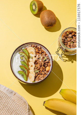 Homemade granola with banana, kiwi and nuts in a bowl on a yellow background with fresh fruits. 118917376