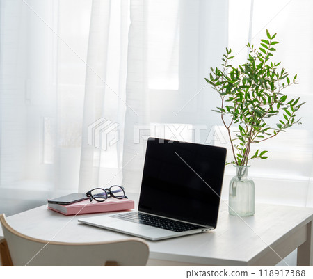 Desktop with laptop, notepad, phone and glasses in front of a window with morning sunlight. 118917388