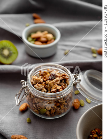 Homemade granola in a jar on a dark linen background with nuts and fruits close up. Homemade granola in a jar on a dark linen background with nuts and fruits close up. 118917395