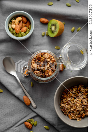Homemade granola in a jar and bowl on a dark linen background with nuts and fruits. 118917396