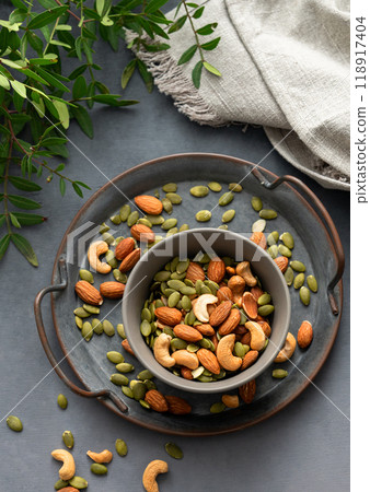 Mix of nuts. Almonds, cashews and pumpkin seeds in a bowl on a dark background with green branch. Mix of nuts. Almonds, cashews and pumpkin seeds in a bowl on a dark background with green branch. 118917404