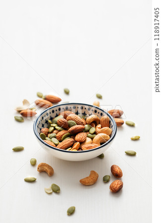 Mix of nuts. Almonds, cashews and pumpkin seeds in a bowl and scattered on a white wooden background Mix of nuts. Almonds, cashews and pumpkin seeds in a bowl and scattered on a white wooden background 118917405