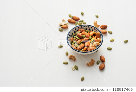 Mix of nuts. Almonds, cashews and pumpkin seeds in a bowl on a white wooden background. Mix of nuts. Almonds, cashews and pumpkin seeds in a bowl on a white wooden background. 118917406