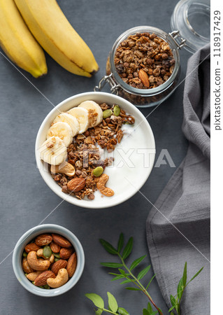 Healthy breakfast. Flat lay of homemade granola with banana and nuts in a bowl on a dark background. Healthy breakfast. Flat lay of homemade granola with banana and nuts in a bowl on a dark background. 118917429