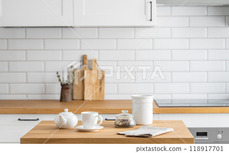 Wooden oak table with a cup of tea and a kettle  in front of the kitchen with a white  background. 118917701