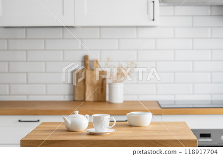 Wooden oak table with a cup of tea and a kettle in front of the kitchen with a white background 118917704