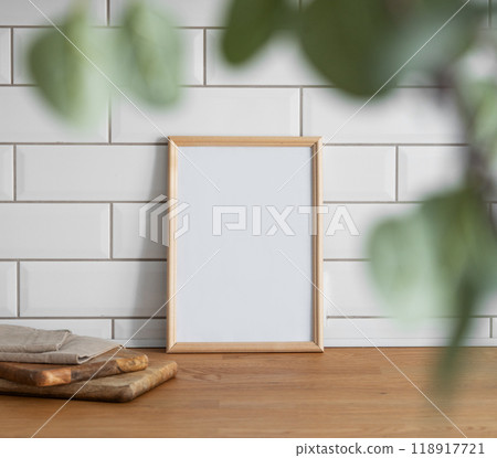 A light frame with a blank canvas against a white tile wall and on a wooden tabletop 118917721