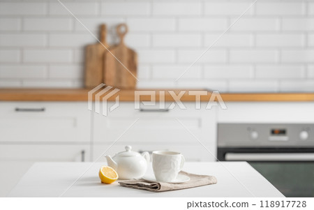 A cup of tea with lemon and a teapot on a white table. A cup of tea with lemon and a teapot on a white table. 118917728