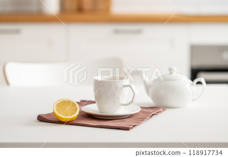 A cup of tea with lemon and a teapot on a white table. Kitchen with wooden empty countertop A cup of tea with lemon and a teapot on a white table. Kitchen with wooden empty countertop 118917734