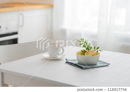 A cup of tea with lemon and a teapot on a white table against the background of a white kitchen A cup of tea with lemon and a teapot on a white table against the background of a white kitchen 118917746