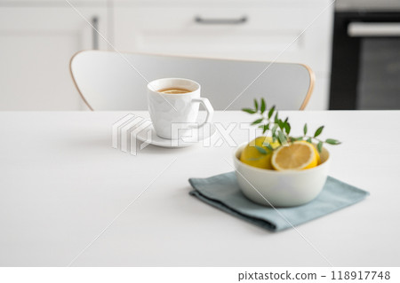 A cup of tea with lemon and a teapot on a white table against the background of a white kitchen. 118917748