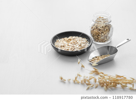 Oatmeal in a plate, jar and in a scoop on a white textured background with dry branch. 118917780