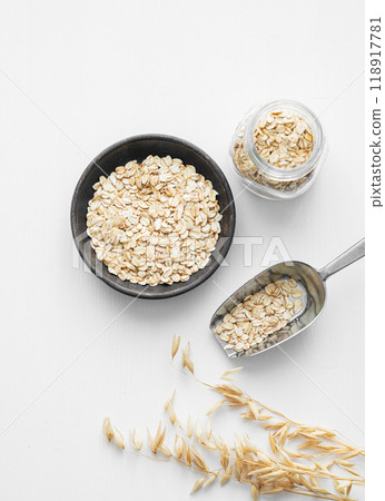 Oatmeal in a plate, jar and in a scoop on a white textured background with dry branch. Oatmeal in a plate, jar and in a scoop on a white textured background with dry branch. 118917781