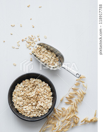 Oatmeal in a plate and in a scoop on a white textured background with dry branch. Oatmeal in a plate and in a scoop on a white textured background with dry branch. 118917788