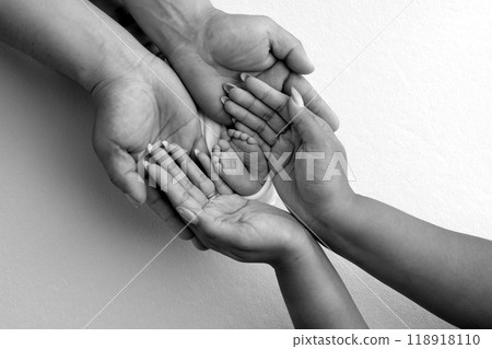 The palms of the parents. A father and mother hold the feet of a newborn child in a blanket. The feet of a newborn in the hands of parents. Black and white Photo of foot, heels and toes 118918110